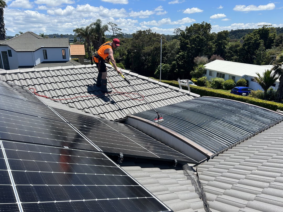 Mike cleaning black roofing iron with a brush on a roof.