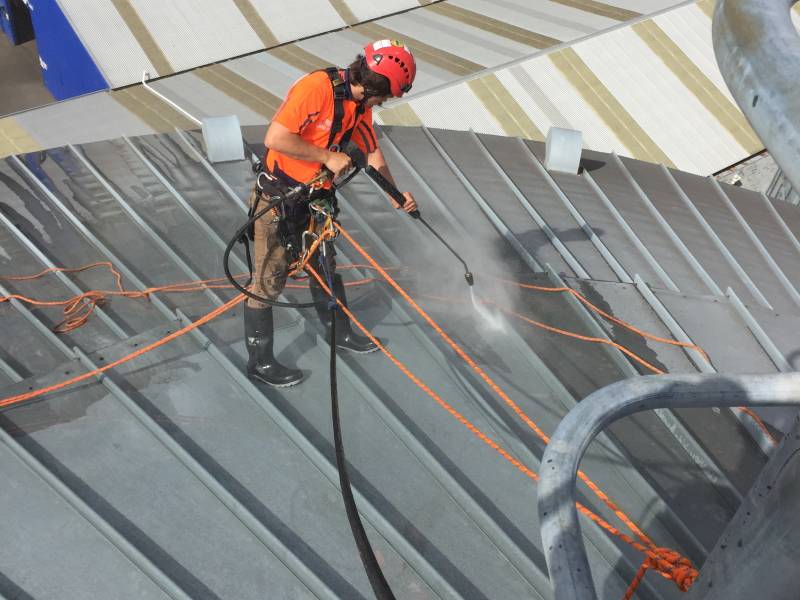 A man water blasting a roof in overalls.